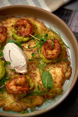 A Close-Up View of Crispy Potato Cakes Topped with Flavorful Shrimp and Creamy Sauce, Garnished with Fresh Herbs and Vibrant Green Puree