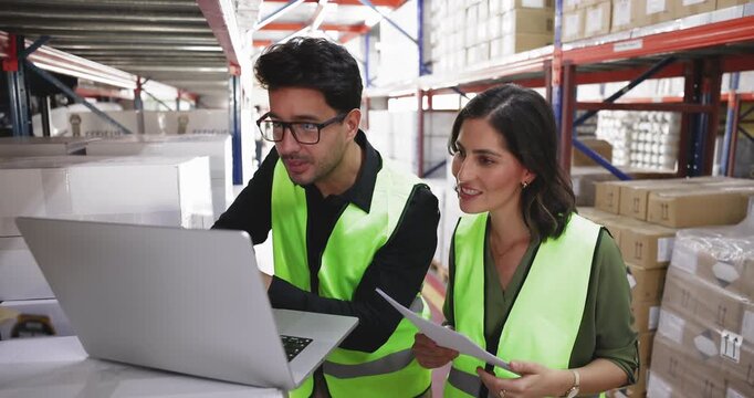 Colleagues standing in warehouse analyzing logistics or inventory-related data using laptop, reviewing shipping or stock reports, discussing products information, collaborating on storage organization - Powered by Adobe