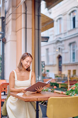 Happy customer choosing meal in restaurant menu sitting at table in outdoor cafe in city street