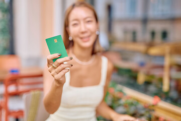 Smiling woman making a contactless payment with her credit card while enjoying a coffee in an outdoor cafe during summer