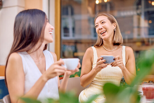 Two female friends enjoying a leisurely afternoon at a cafe, sipping coffee, sharing laughter, and engaging in lively conversation