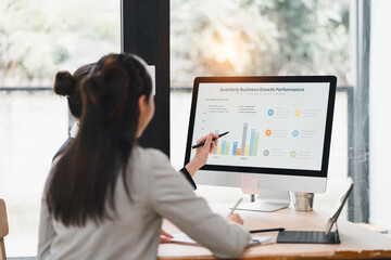Two businesswomen analyzing quarterly business growth performance on computer screen, discussing data and charts in modern office, teamwork and collaboration concept