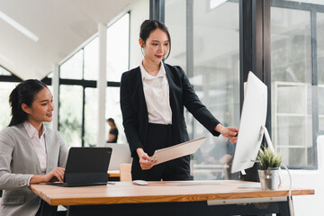 Two businesswomen working together in modern office, one using tablet and other pointing at...