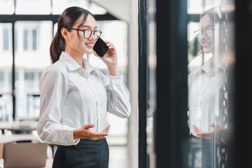 Smiling businesswoman office glasses white shirt black pants standing talking on smartphone...