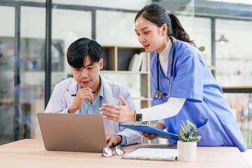 Two Asian medical professionals, male doctor and female nurse, collaborate at desk with laptop,...