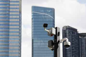 Security cameras on pole with modern building in background.