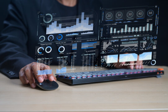 A person interacts with a futuristic transparent digital interface displaying various data charts and graphs above a keyboard and mouse.