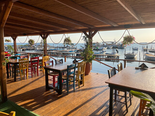 Cozy seaside restaurant terrace with colorful chairs and wooden tables, overlooking a peaceful...