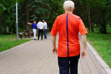 Older man walks through a park during daytime while others engage in conversation in the background