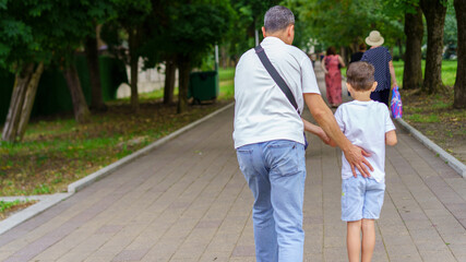 Elderly man walking with young boy in park during sunny day