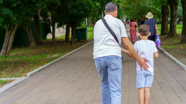 Elderly man walking with young boy in park during sunny day