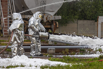 Firefighters in protective clothing use a foam generator to supply foam to extinguish the fire. Foam fire extinguishing technology. The rescue service. Firefighters extinguish the fire.