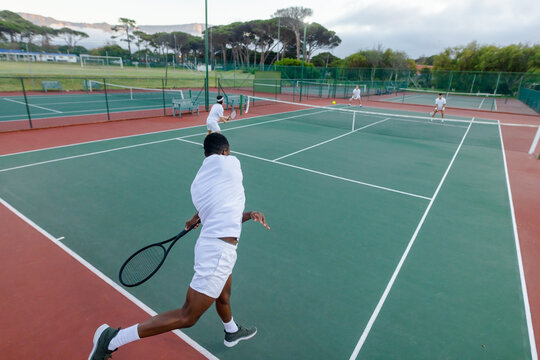 Diverse male tennis players competing intensely on outdoor hard court with rackets, ball and net