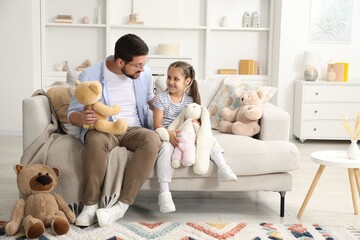 Father and his daughter playing with stuffed animals on sofa at home