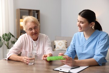 Nurse giving pills to senior woman at wooden table indoors. Home health care service