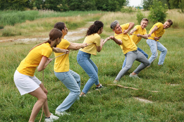 Fototapeta premium Team building. Group of happy people playing tug of war with rope outdoors
