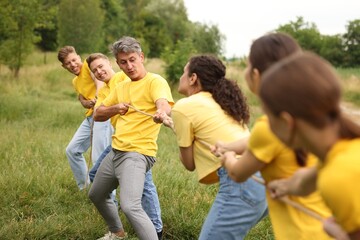 Fototapeta premium Team building. Group of happy people playing tug of war with rope outdoors