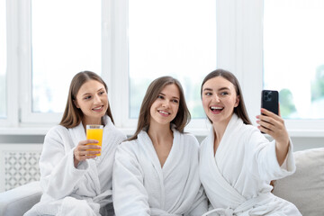 Happy women in bathrobes taking selfie in spa salon