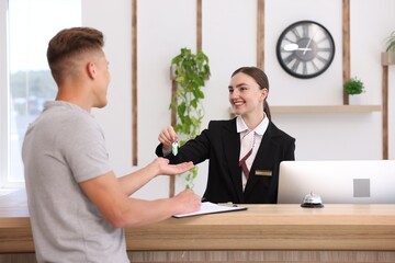 Smiling receptionist in uniform giving guest room key to client at reception desk in hotel