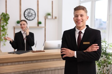 Smiling receptionist in uniform and his colleague working in hotel, selective focus