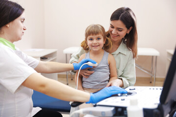 Sonographer conducting ultrasound examination of girl's heart. Mother and daughter having...