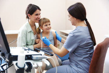 Sonographer conducting ultrasound examination of girl's heart. Mother and daughter having...