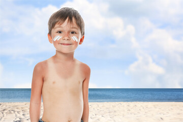 Little boy with sunburned skin on beach. Soothing cream on his cheeks