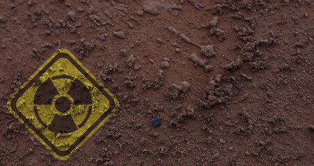 Yellow radioactive sign on brown ground, top view. Radiological pollution