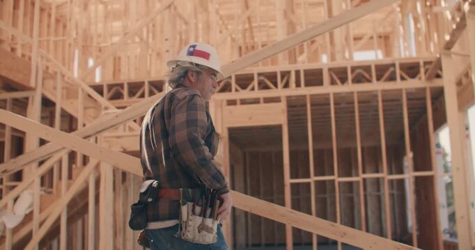 Construction Worker Wearing Hard Hat With Texas Flag Stickers Walking and Looking Around Inside of Wooden Frame of House at Construction Site