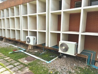 Two outdoor air conditioning units are situated beneath a building's unique facade, featuring a...