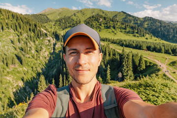 Young hiker taking selfie portrait with beautiful mountain landscape in background during summer...