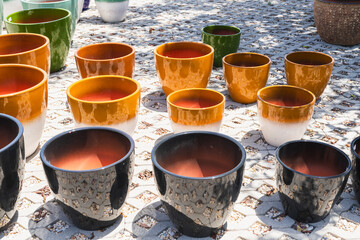 Black and orange ceramic pots with ombre and textured finishes are arranged in sunlight on a patterned tile surface.