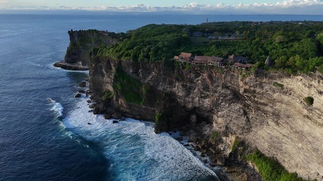 Aerial drone footage gliding over Pura Luhur Uluwatu dramatic cliffs, lush green hills, and  ocean shore. Bali, Indonesia