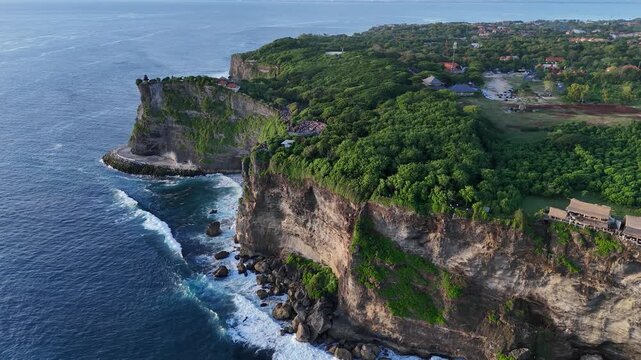 Aerial drone footage gliding over Pura Luhur Uluwatu dramatic cliffs, lush green hills. Bali, Indonesia	