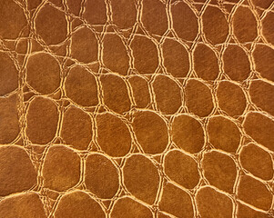 Close up of crocodile skin leather in bright golden brown color. Exotic leather texture resembling reptile scales or skin. Seamless background texture.
