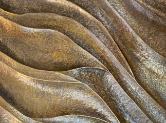 Close up of decorative leaves and wavy 3D carved panel in gold and brown metallic paint finish. 3d antique craft made of wrought iron with rough golden brown textured paint. Seamless background.