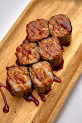 A Delicious Platter of Sushi Rolls Drizzled with Savory Sauce Served on a Wooden Platter, Perfectly Showcasing Culinary Craftsmanship and Artistry.