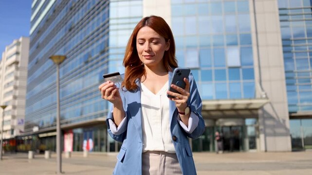 Professional businesswoman standing near sleek architecture, processing digital payment using smartphone and credit card