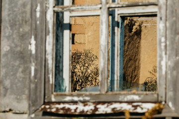An old wooden abandoned house with broken windows stands in a field among overgrown grass on a summer day against a clear and clear blue sky with clouds. the texture of an old house