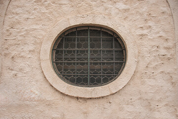 Old round window with metal bars on a textured stone wall