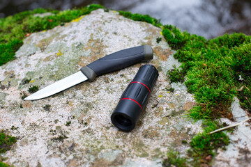 camping knife and monocular on a stone near a river
