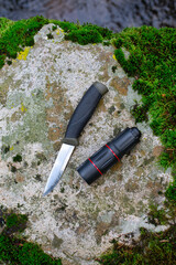 camping knife and monocular on a stone near a river