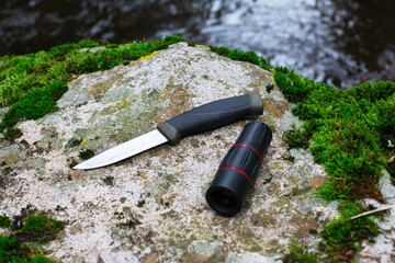 camping knife and monocular on a stone near a river