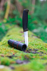 camping knife and monocular in a log covered with moss in the forest
