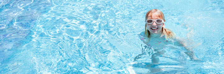 Cheerful girl in swim goggles smiling in bright blue pool water. Horizontal wide format with copy space. Great for travel, wellness, or swim school themes