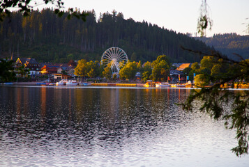 view on the lake coast with Ferris wheel and mountain forest at sunset