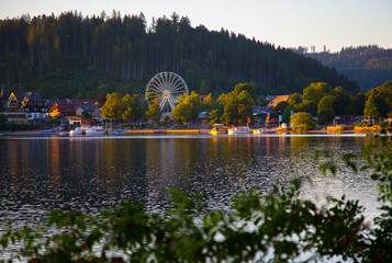 view on the lake coast with Ferris wheel and mountain forest at sunset