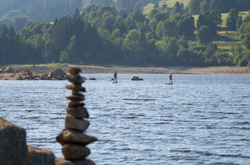 unrecognisable people on sup boards on the lake with forest coast in sunlight