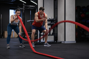 Young woman exercising with battle ropes and professional personal trainer in gym
