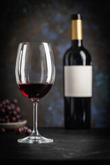 A dark, elegant still life of red wine in a glass with wine bottles and fresh grapes in the background. Perfect for wine-themed compositions